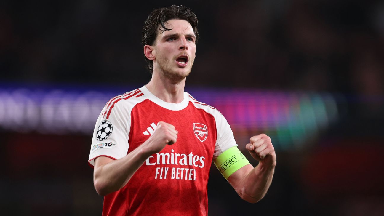 -  Arsenal captain in red and white jersey with Emirates Fly Better, fists clenched in celebration on the pitch, wearing a captain's armband.